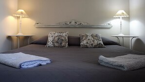 Una cama bien hecha con dos almohadas, dos mesitas de noche con lámparas y una pequeña estantería sobre la cama.