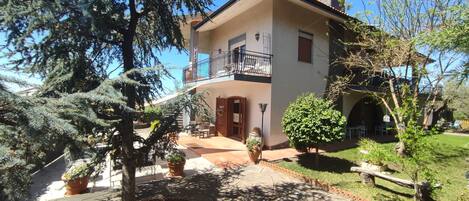 A two-story house with a balcony, potted plants, and a well-maintained garden.
