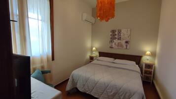 A bedroom with a bed, bedside lamps, a wall-mounted air conditioner, and a window with curtains.