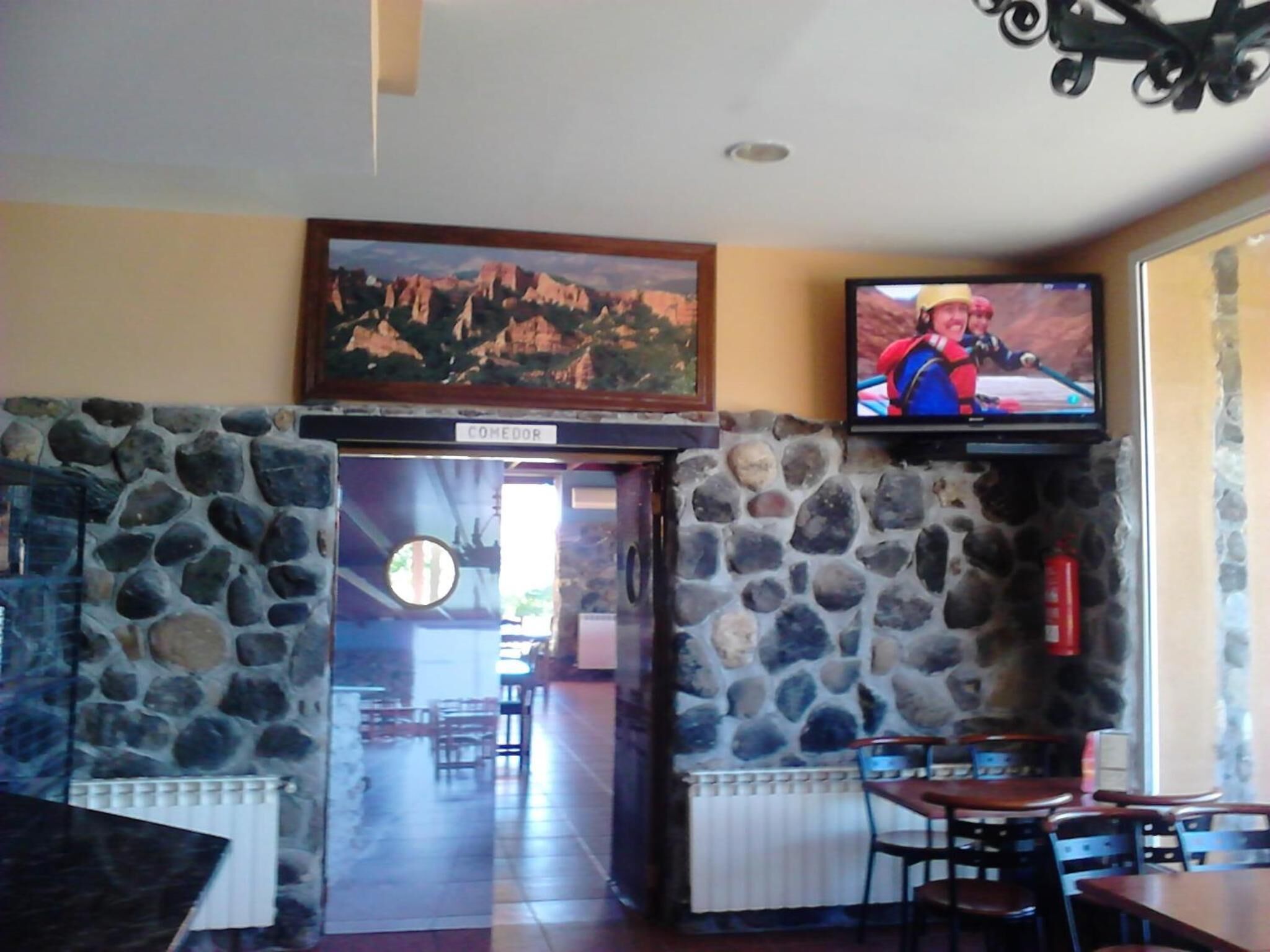 A restaurant with stone walls, a mounted painting, and a television screen displaying a person in a red jacket.