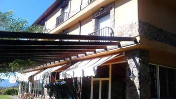 A two-story building with a stone facade, a covered patio with outdoor seating, and a view of the mountains in the background.