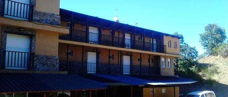 Un edificio de varios pisos con balcones, una zona de estacionamiento techada y una camioneta estacionada afuera.