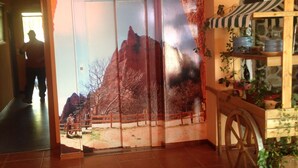 A room with a large door leading to an outdoor area, a wooden cart with plants, and a painting on the wall. - Hotel Medulio (Carucedo)