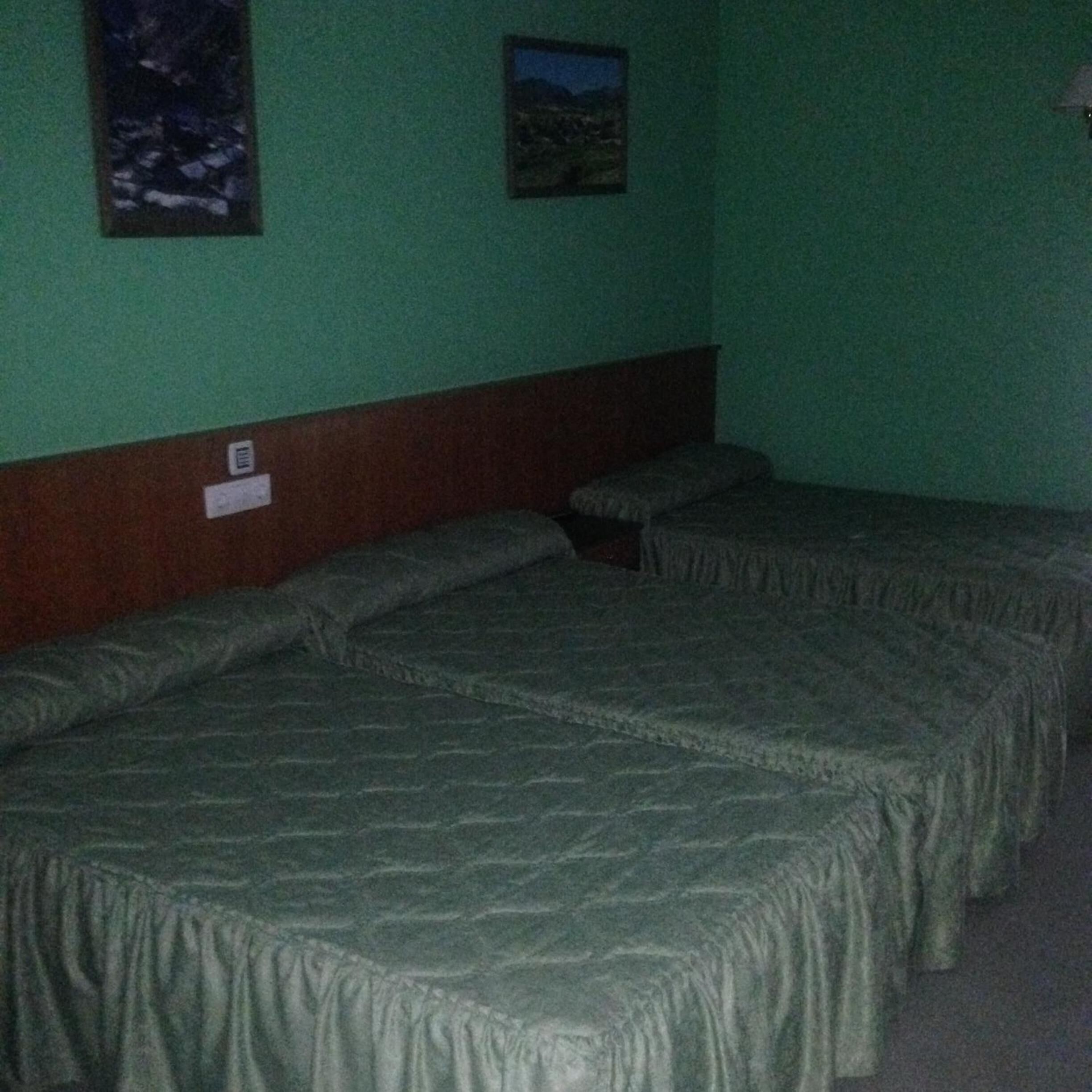 A room with three single beds, a wooden headboard, and two framed pictures on the wall.