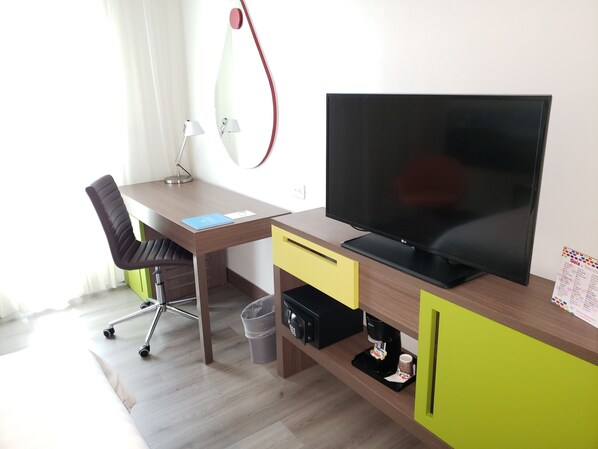 Una habitación moderna con un escritorio de madera, un televisor negro, una silla, una lámpara y una cafetera.