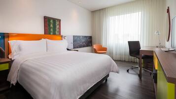 A hotel room with a large bed, a desk, an orange chair, and a painting on the wall.