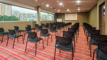 A conference room with rows of chairs, a projector screen, and a large window with a city view.