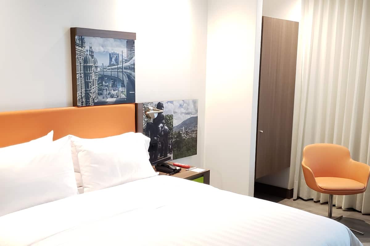 A hotel room with a large bed, a nightstand, a chair, and two wall art pieces.