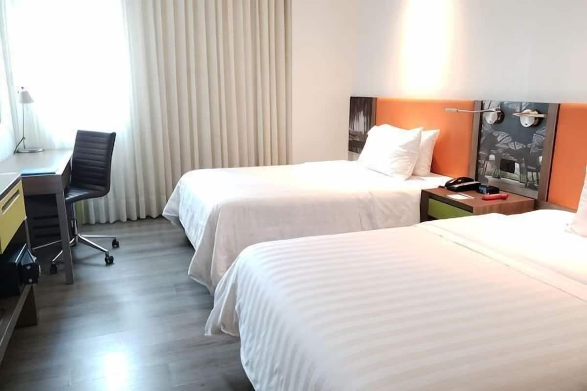 A hotel room with two beds, a desk, a chair, and a nightstand.