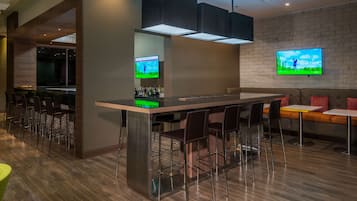 Un espace bar moderne avec un long comptoir, des tabourets de bar et un téléviseur fixé au mur diffusant un tournoi de golf.