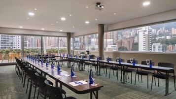 A conference room with long tables, chairs, and blue glassware, featuring large windows and a city view.
