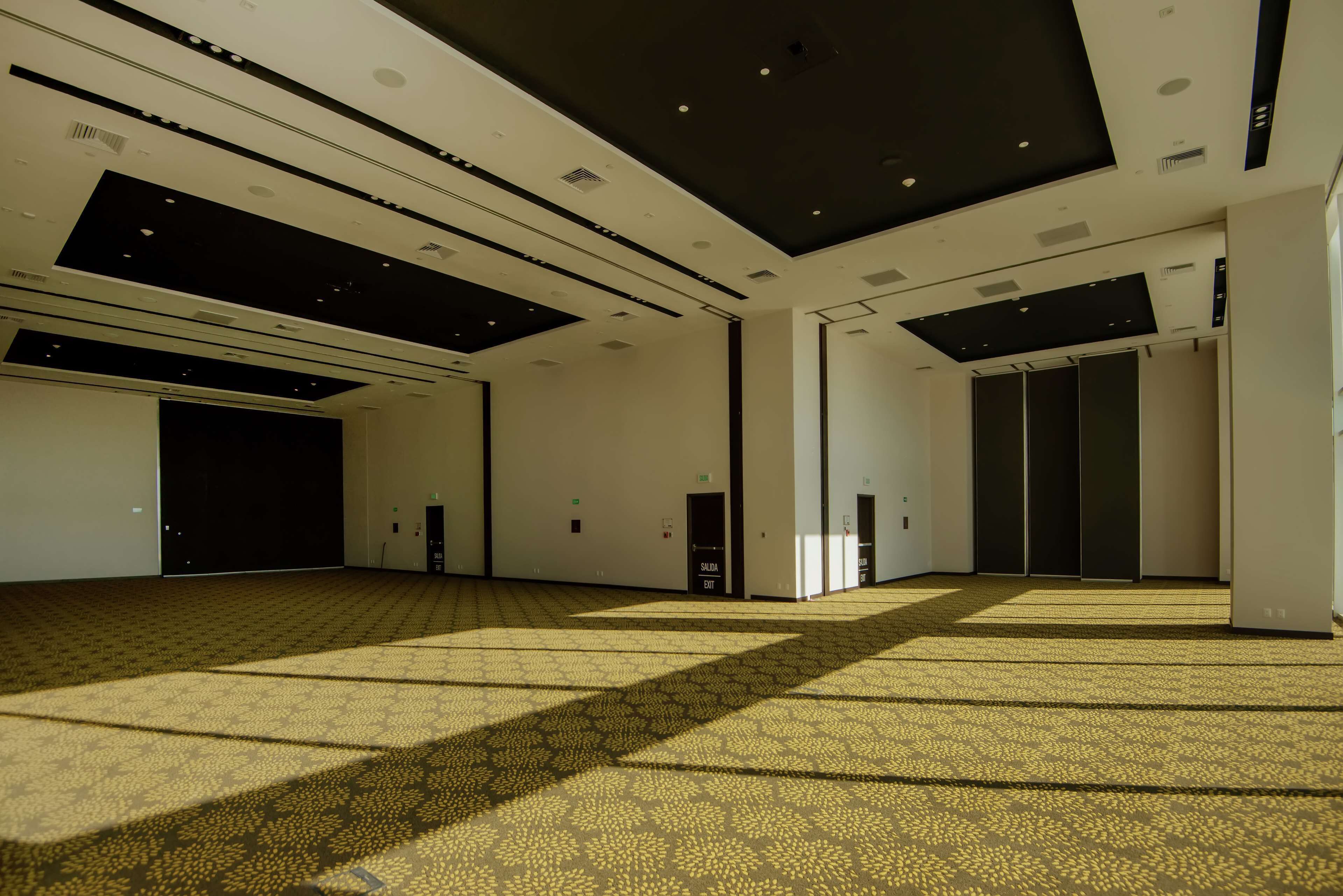 A spacious, modern hotel lobby with a patterned carpet, recessed lighting, and a high ceiling.