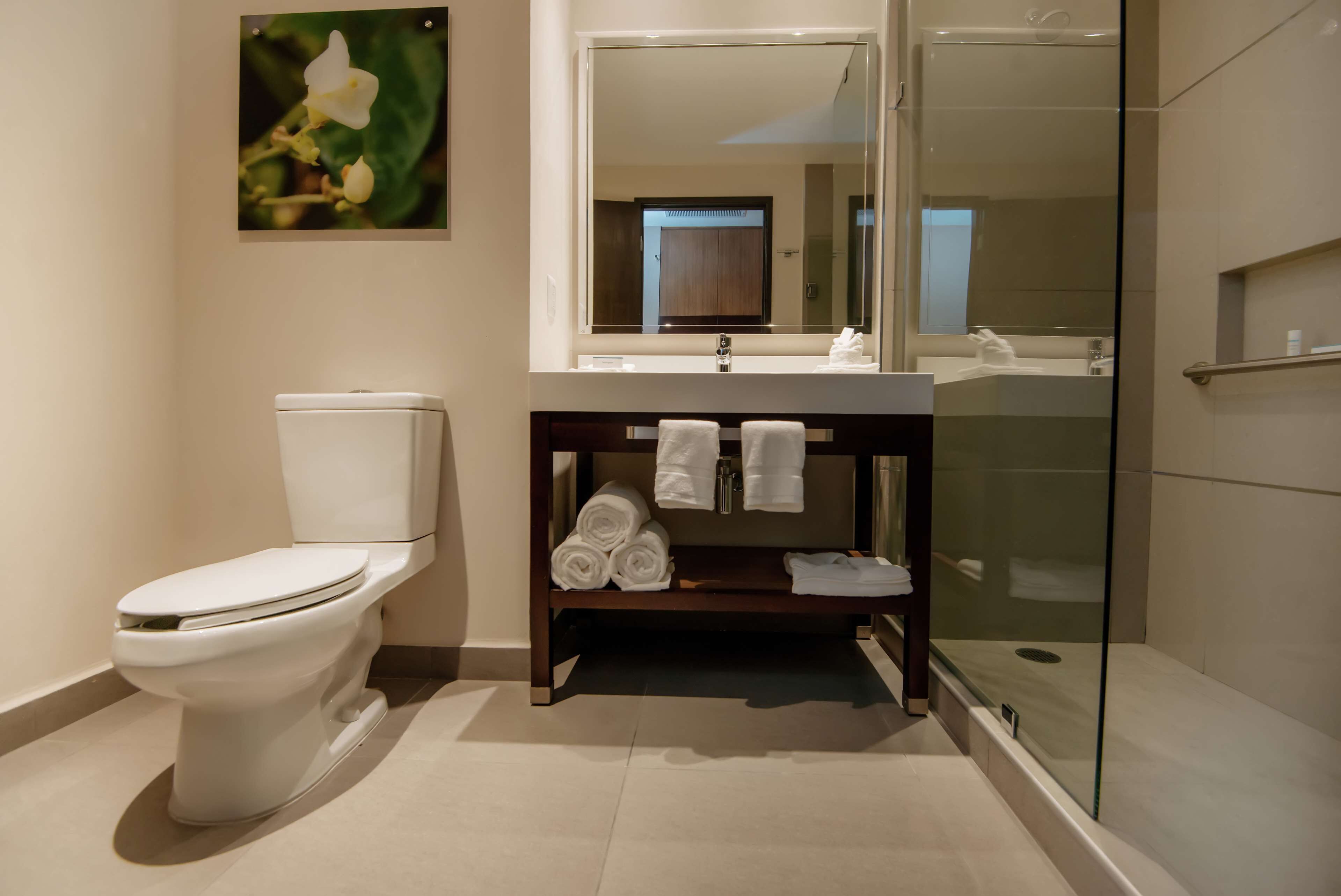 A modern bathroom with a toilet, a sink, a glass shower enclosure, and a towel rack with towels.