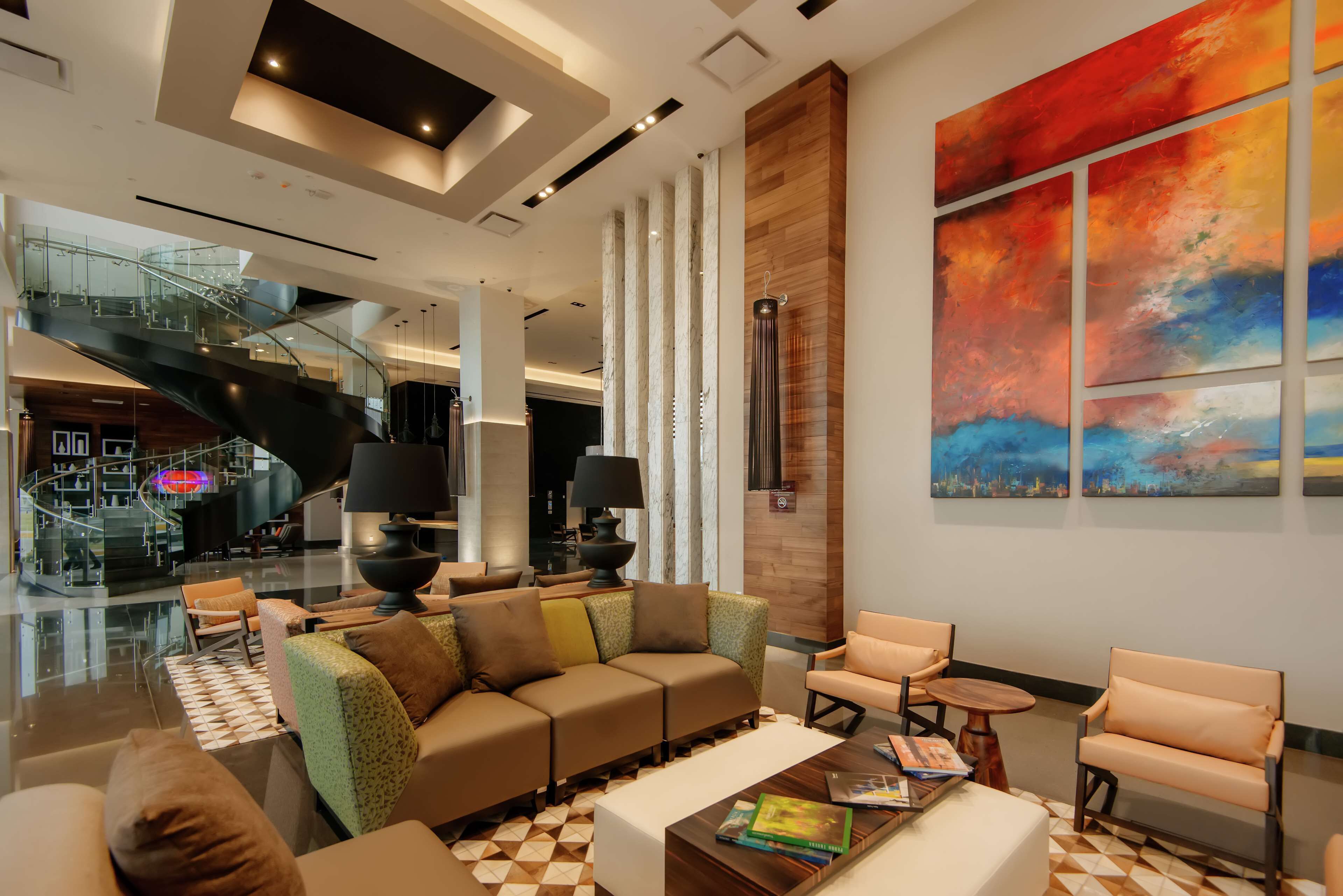 A modern lobby with a curved staircase, a large abstract painting, and a seating area with sofas and armchairs.