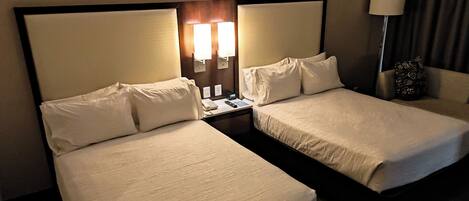 Une chambre d’hôtel avec deux lits simples, une table de chevet avec un téléphone et une lampe, et un luminaire fixé au mur.
