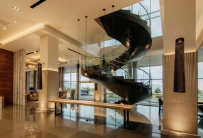 Un moderno vestíbulo de hotel con una escalera espiral central, ventanas amplias y un suelo pulido.