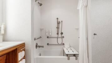 Un baño moderno con ducha a nivel, barras de apoyo, una bañera blanca y un mueble de tocador de madera con toallas.