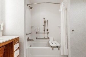 Un baño moderno con ducha a nivel, barras de apoyo, una bañera blanca y un mueble de tocador de madera con toallas.
