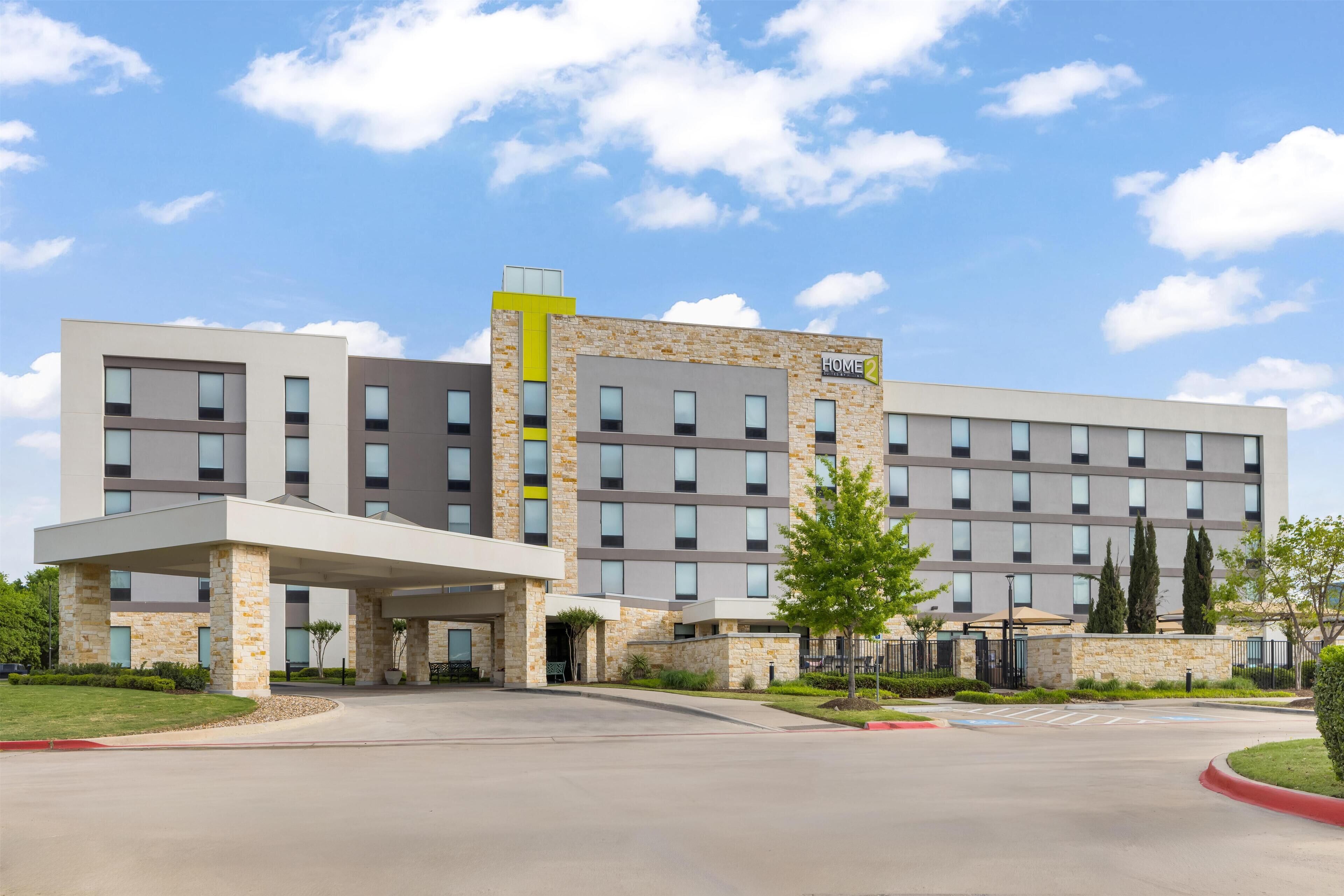 A multi-story hotel with a covered entrance, stone facade, and a clear sky.