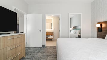 A hotel room with a bed, a TV, a dresser, a bathroom visible through an open door, and a patterned wall.