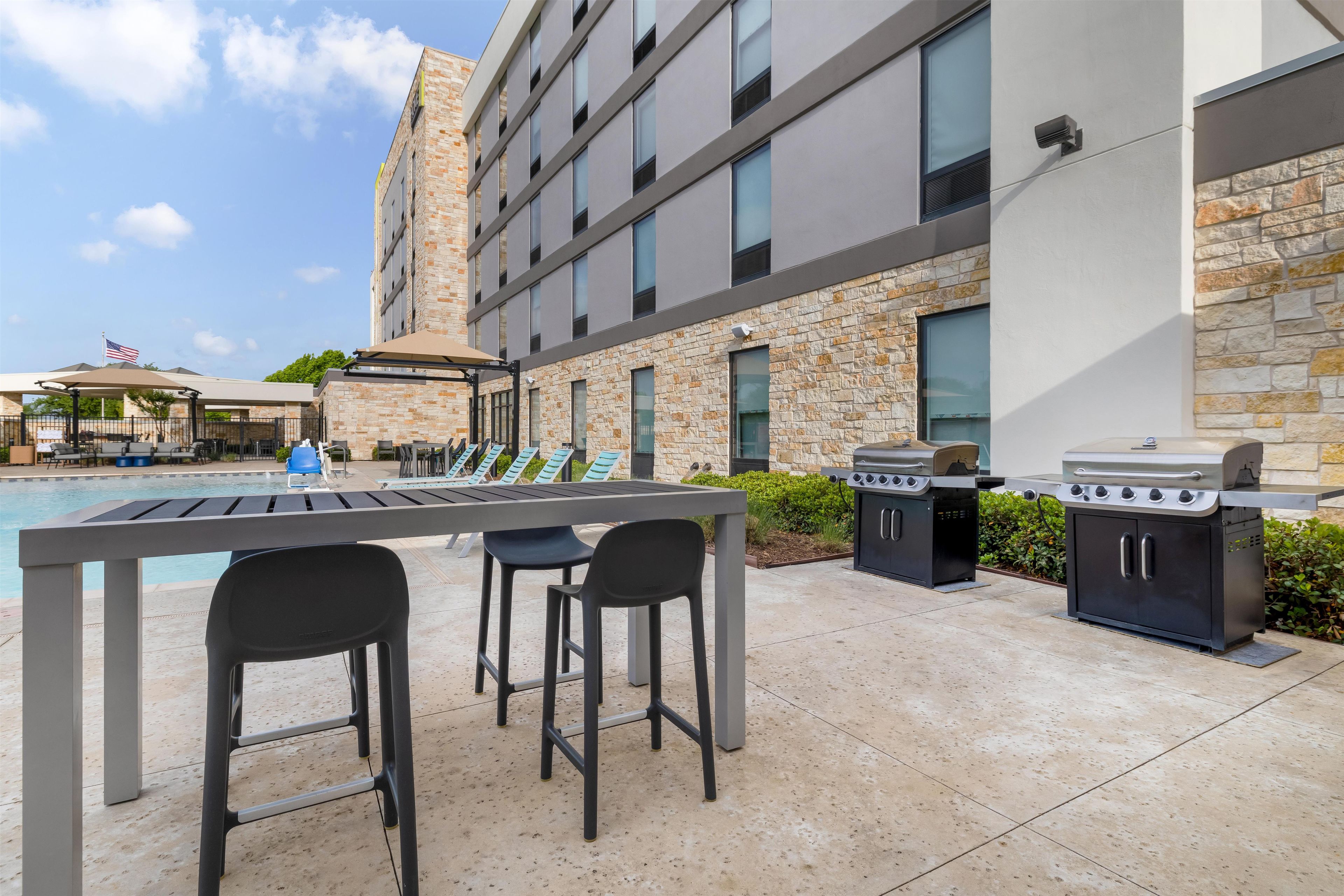 An outdoor pool area with lounge chairs and a barbecue station.