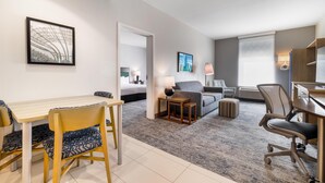 A hotel room with a dining area, a sofa, a desk, and a lamp.