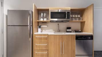A compact kitchen with a stainless steel refrigerator, a microwave, a dishwasher, wooden cabinets, and a countertop with a sink.