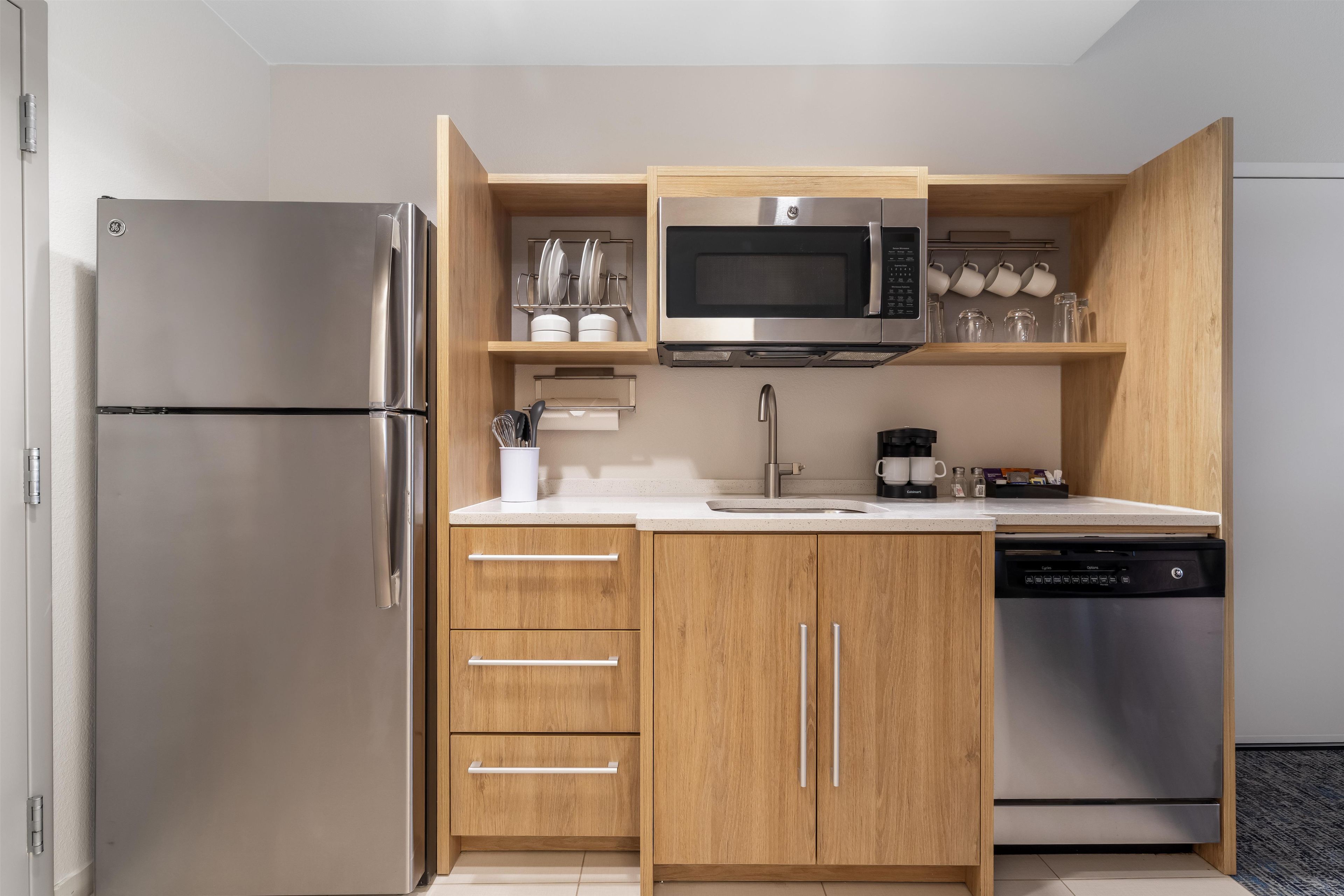 A compact kitchen with a built-in microwave, stainless steel refrigerator, and a dishwasher.