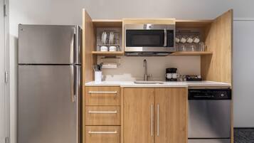 A compact kitchen with a built-in microwave, stainless steel refrigerator, and a dishwasher.