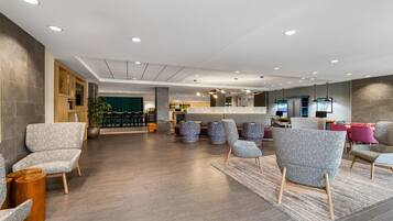 A modern lobby with seating areas, a reception desk, and a green curtain backdrop.
