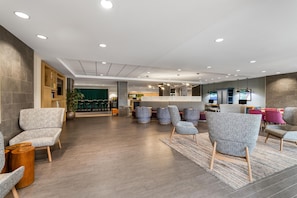 A modern lobby with seating areas, a reception desk, and a green curtain backdrop. - Home2 Suites by Hilton Dallas Addison (Addison)