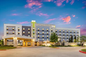 A multi-story hotel with a modern design, featuring a prominent entrance with a covered area and a well-maintained lawn. - Home2 Suites by Hilton Dallas Addison (Addison)