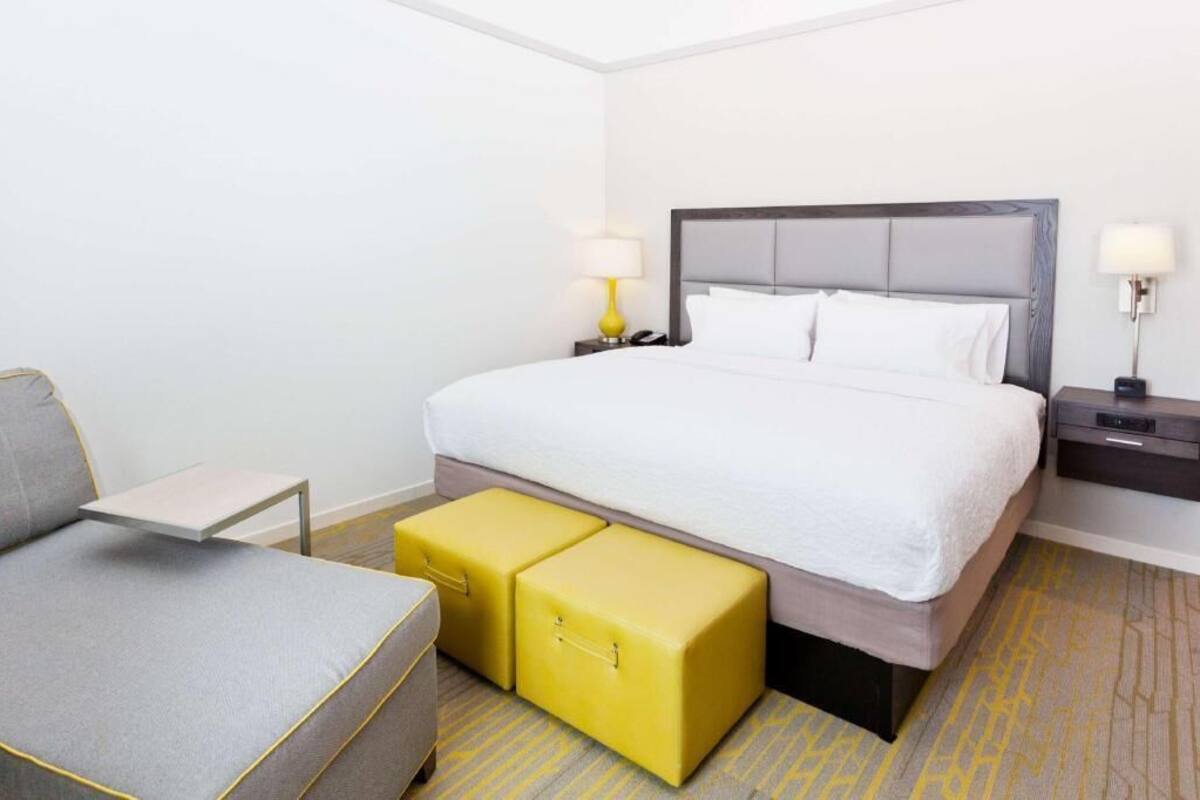 A hotel room with a bed, bedside tables, a small sofa, and two yellow storage units.