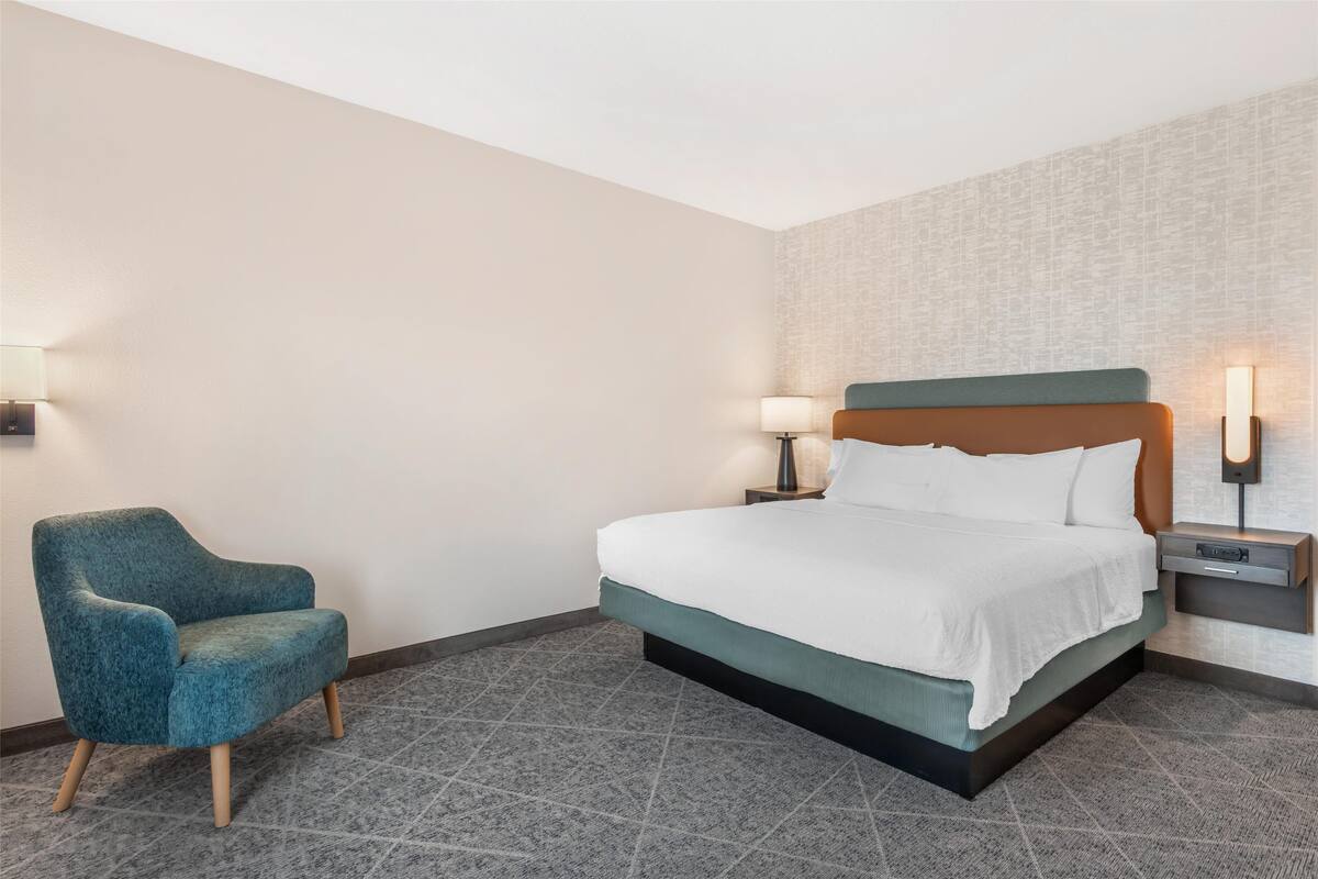 A hotel room with a bed, a chair, and two bedside tables with lamps.