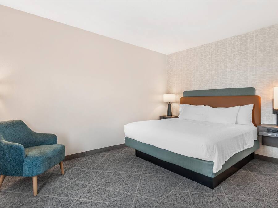 A hotel room with a bed, a chair, and two bedside tables with lamps.