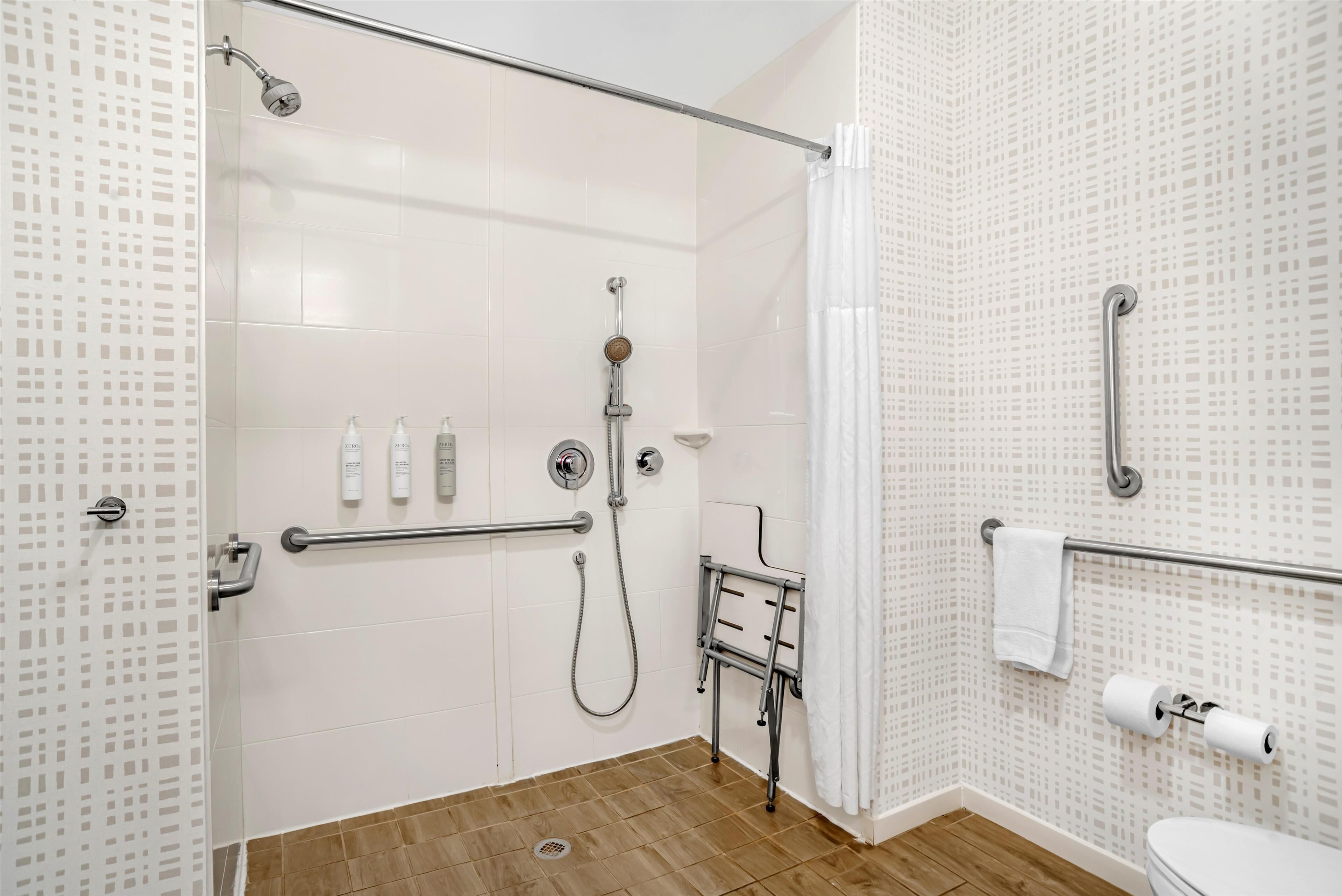 Un baño moderno con ducha, inodoro y barras de apoyo.