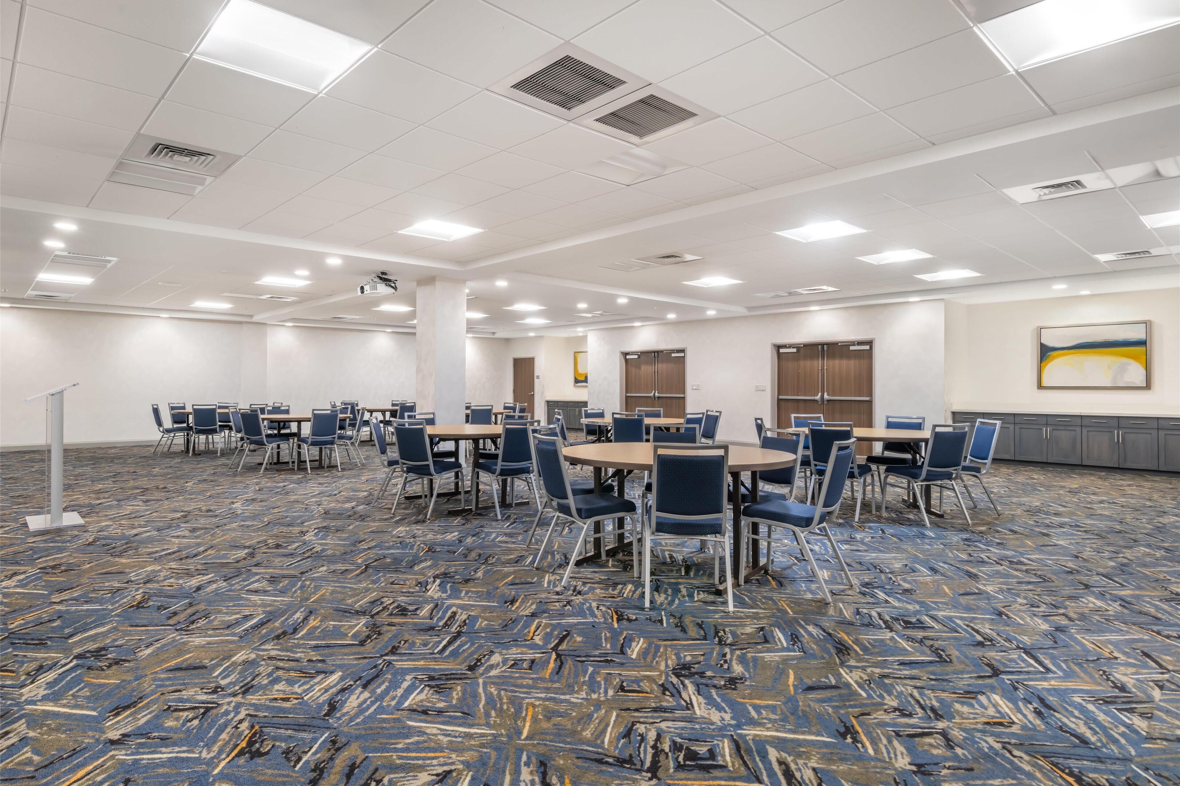 Une salle de conférence avec des tables et des chaises, des murs blancs et un tapis à motifs.