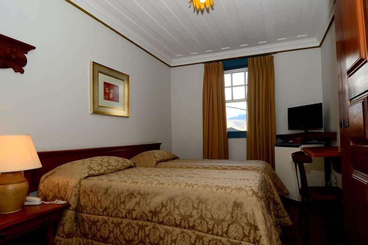 Habitación de hotel con cama, escritorio con televisor, teléfono y ventana con cortinas.