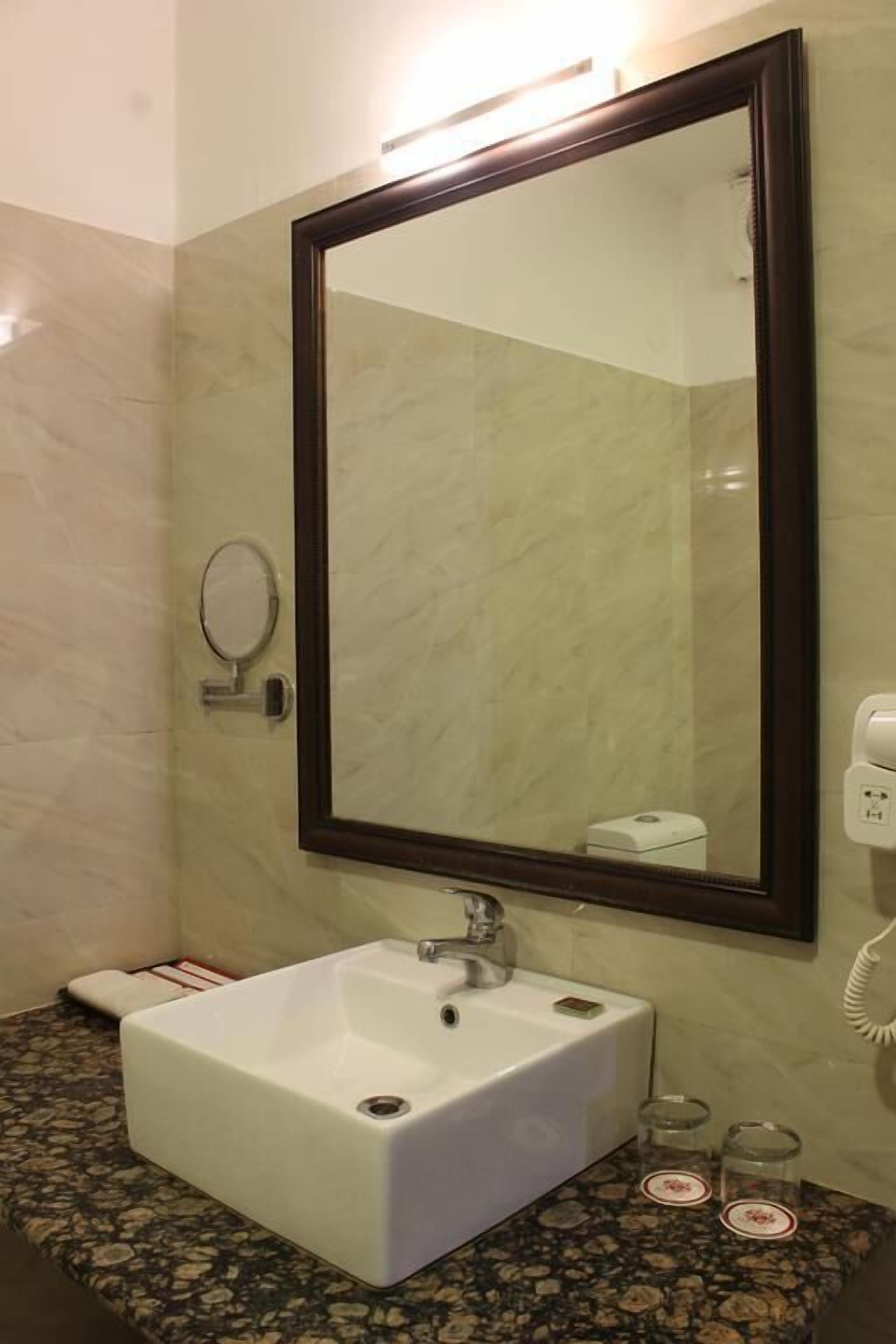 A bathroom with a white sink, a large mirror, a round hand mirror, and a towel rack.