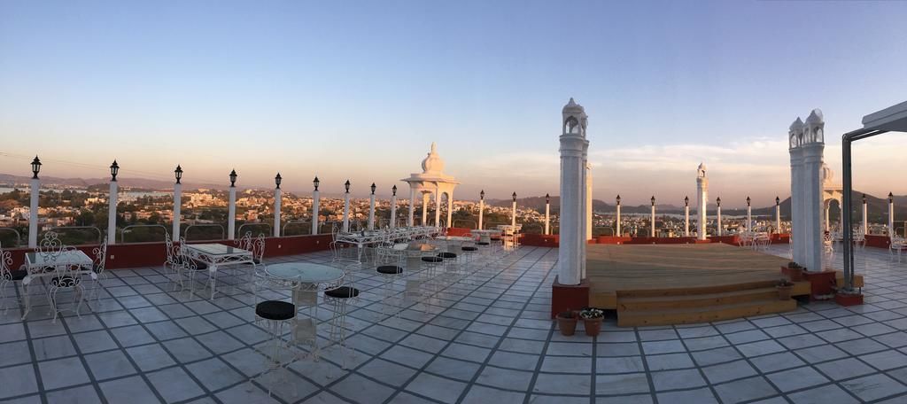 A rooftop terrace with tables and chairs, a white gazebo, and a view of a cityscape in the background.