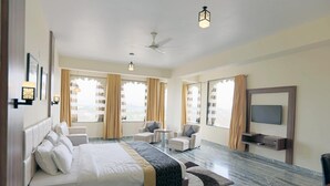A spacious hotel room with a large bed, two armchairs, a small table, a TV, and large windows with curtains. - Regenta Central Mewargarh Udaipur (Udaipur)