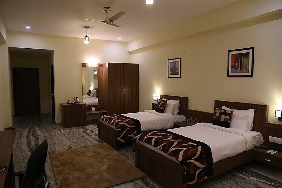 Une chambre d’hôtel avec deux lits, un bureau, une chaise, une armoire et un ventilateur de plafond.