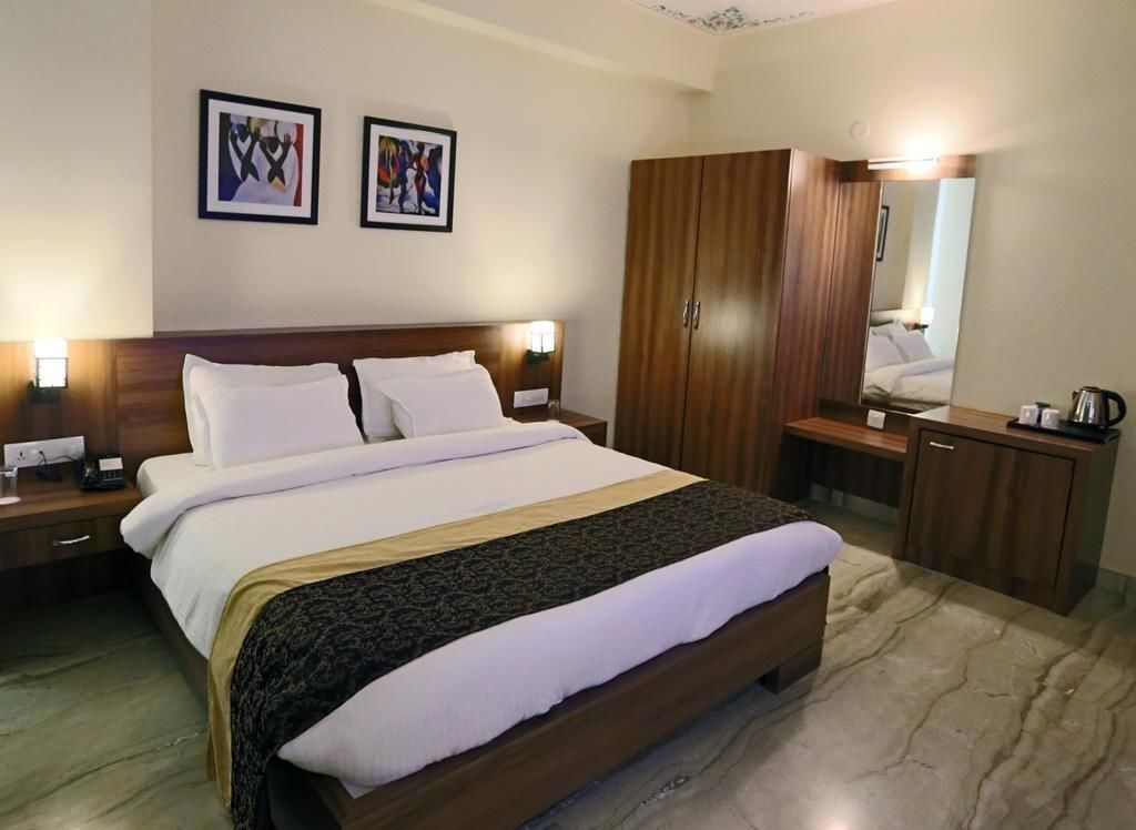 A hotel room with a large bed, wooden wardrobe, bedside table, and a mirror.