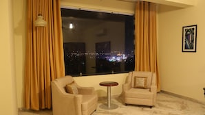 A room with two armchairs and a small round table, a large window with curtains, and a framed picture on the wall. - Regenta Central Mewargarh Udaipur (Udaipur)