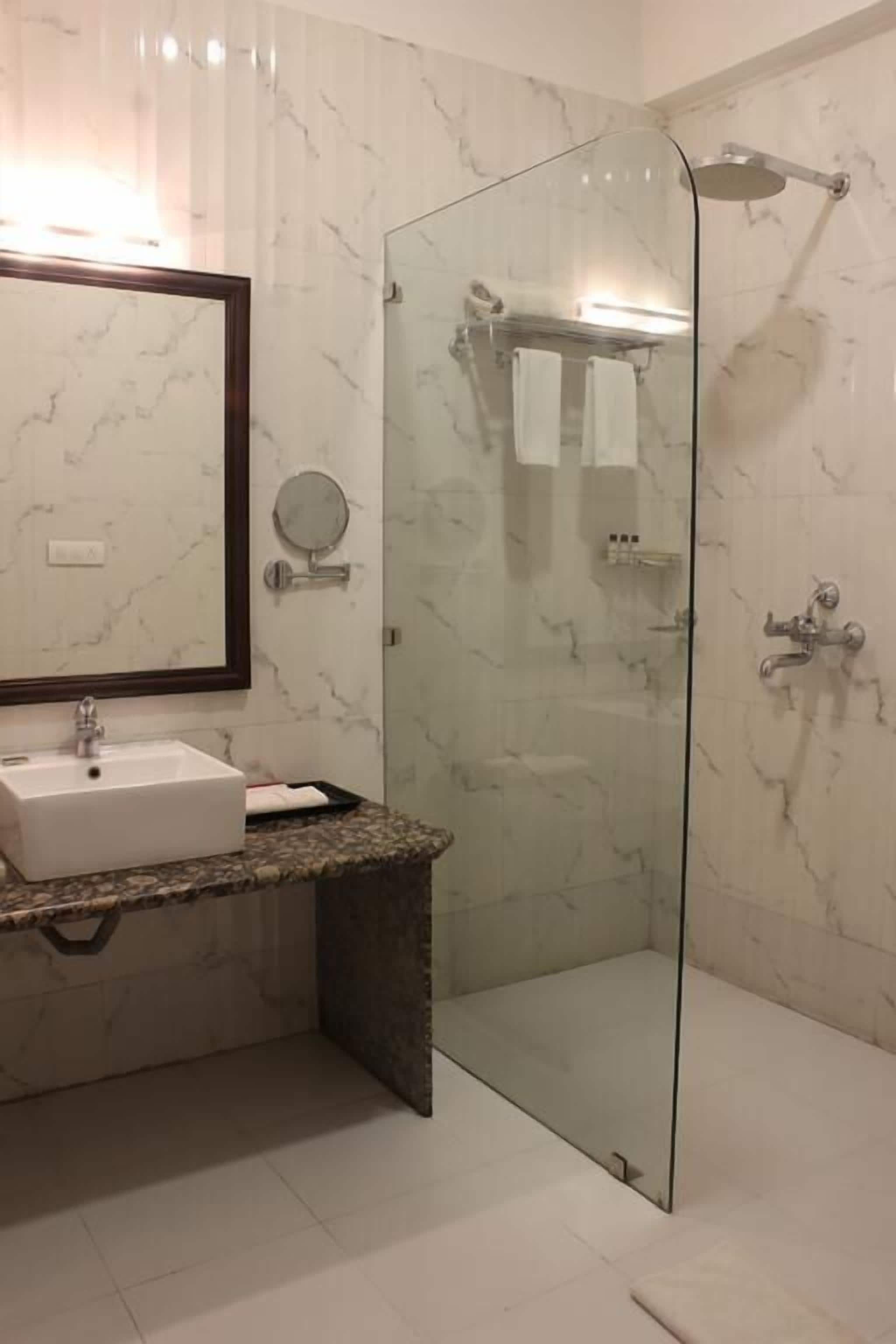 A modern bathroom with a glass shower enclosure, a marble-tiled wall, a sink with a marble countertop, and a large mirror.