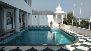 A swimming pool with a checkered floor, a small white structure, and mountains in the background. - Regenta Central Mewargarh Udaipur (Udaipur)