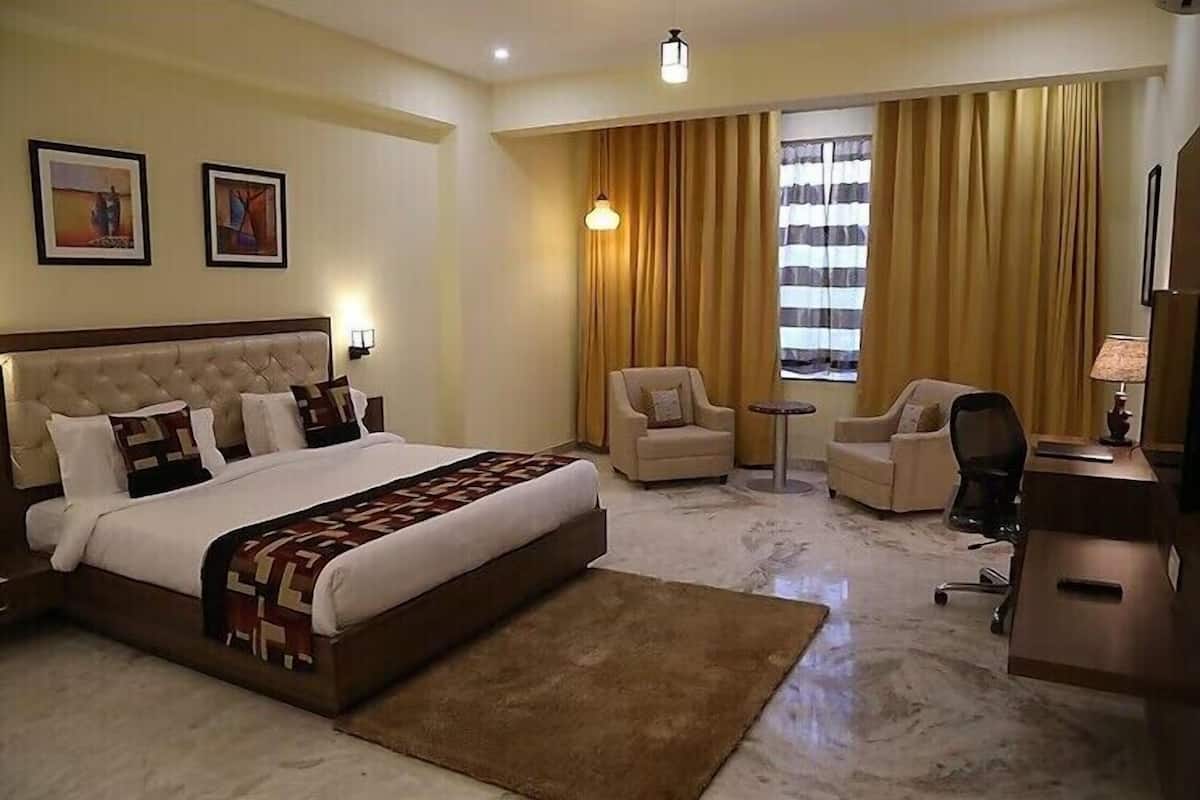 Une chambre d’hôtel avec un grand lit, deux fauteuils, un bureau et une télévision.