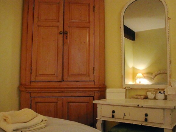 Una habitación con un armario de madera, un tocador blanco con espejo y una cama con una toalla doblada.