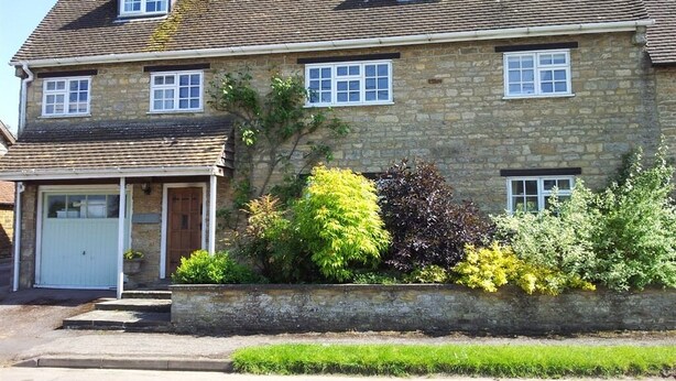 A two-story stone house with a garage, a front porch, and a variety of shrubs and plants. - Stone House Bed and Breakfast (Banbury)