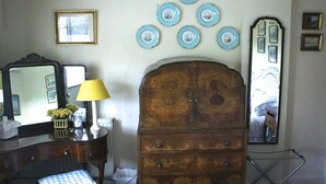 A room with a wooden dresser, a mirror, a lamp, and a blue checkered chair. - Stone House Bed and Breakfast (Banbury)